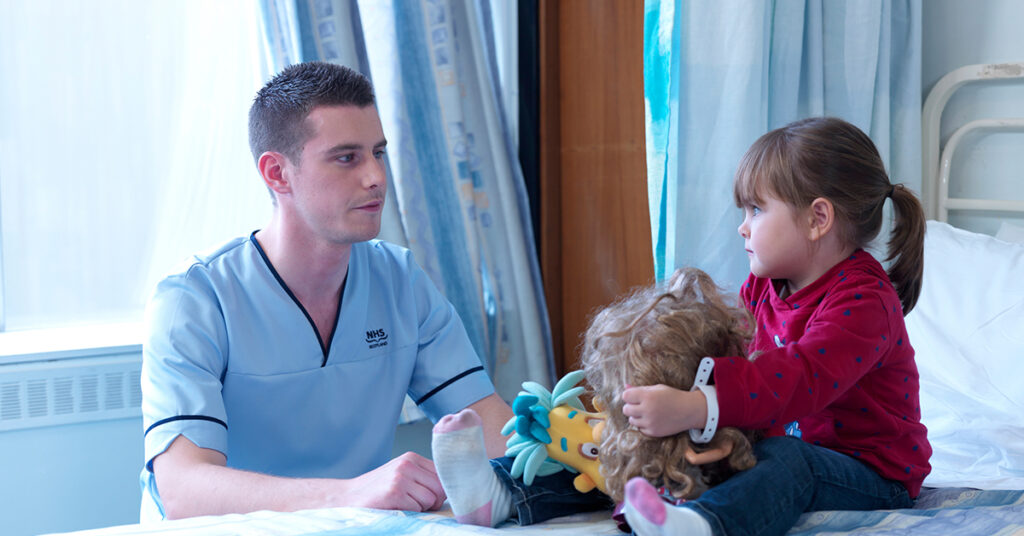 Nurse sitting down next to child patient holding toys