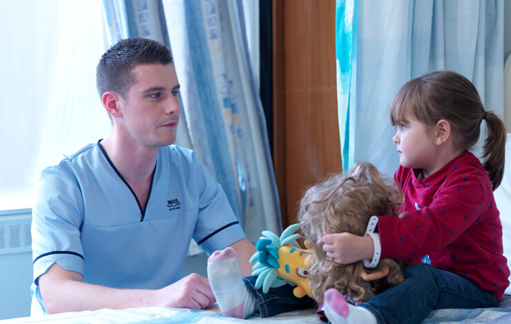 Nurse sitting down next to child patient holding toys