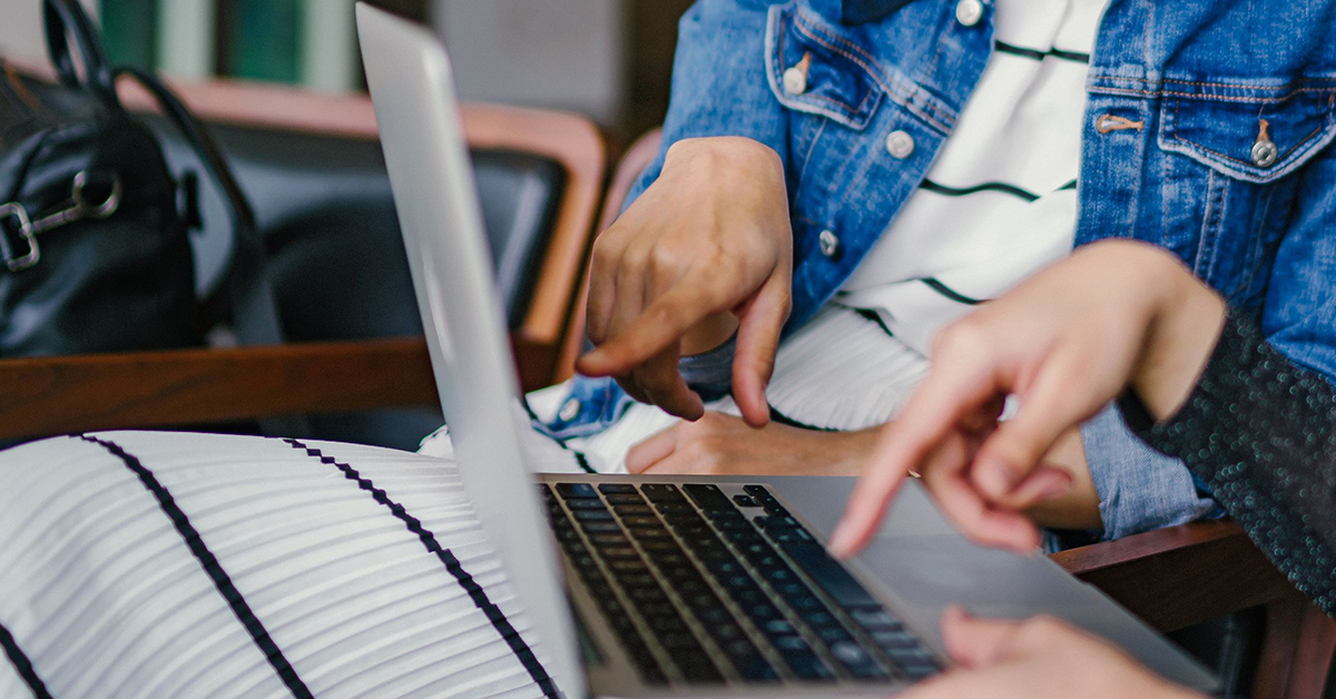 Two people sat down at a laptop pointing at screen