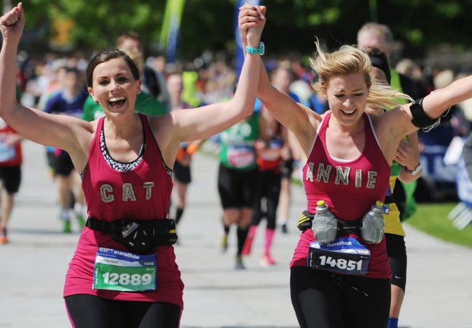 Two girls holding hands in the air smiling as they run the Edinburgh Marathon