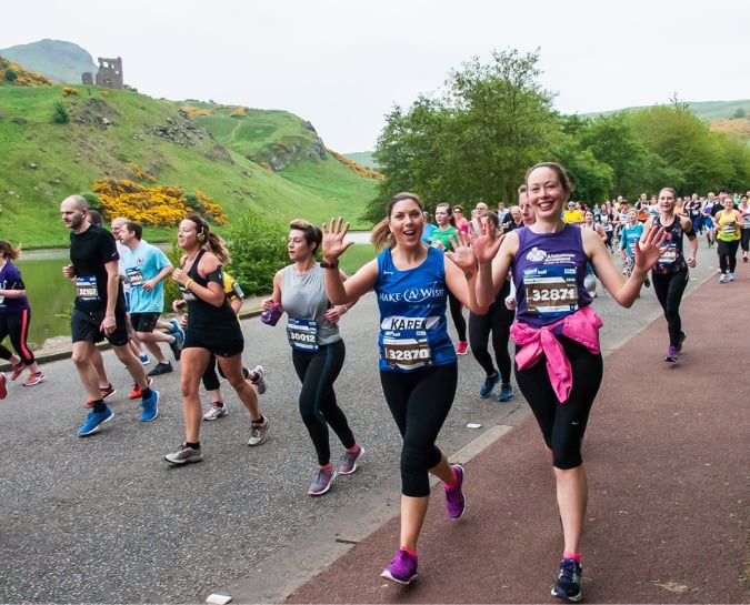 Two girls waving and smiling as they are running the Edinburgh Marathon