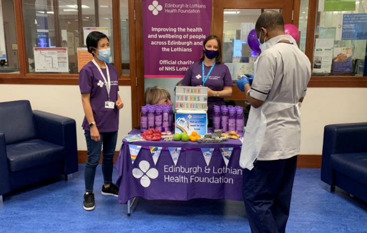 three people beside a table with goodies advertising NHS Big Tea