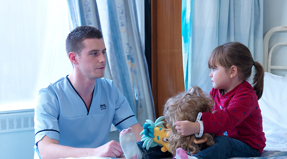 Nurse sitting down next to child patient holding toys
