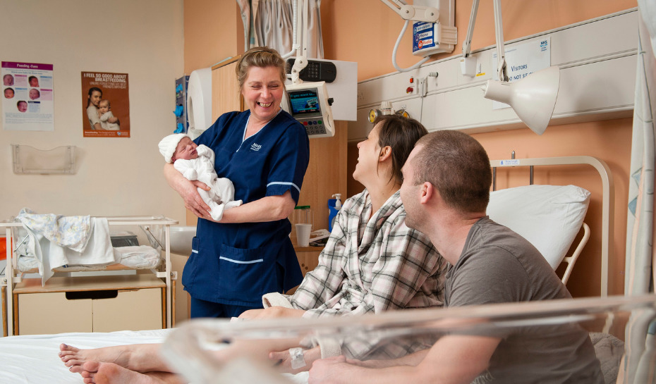 Nurse smiling holding a baby whilst looking at the parents