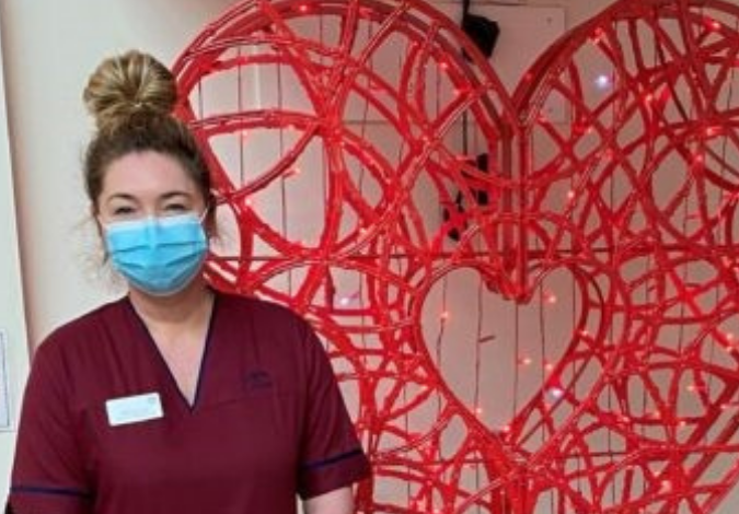 Nurse with face mask standing in front of a large heart sculpture