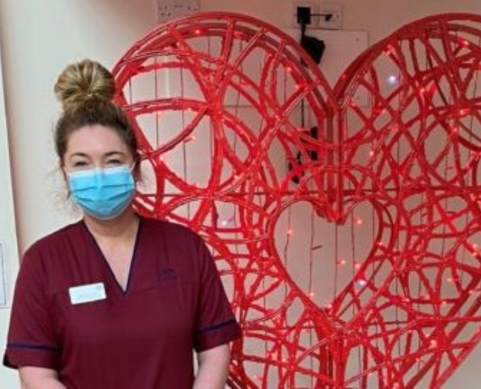 Nurse with face mask standing in front of a large heart sculpture