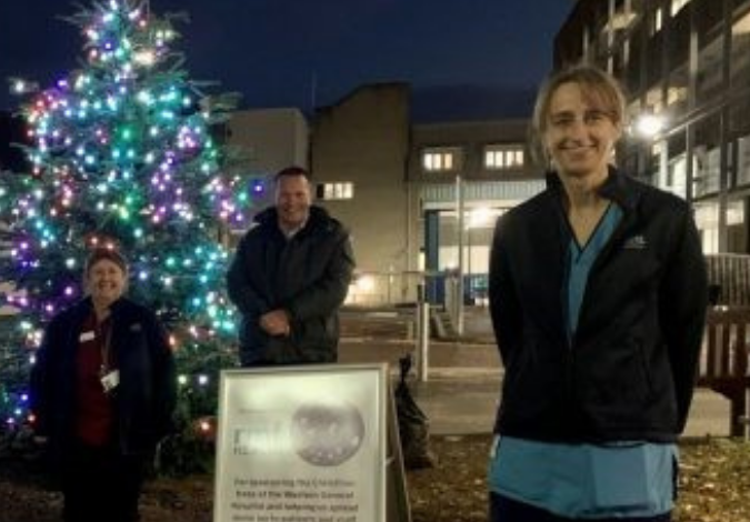 Nurses standing in front of a lit Christmas tree in the hospital grounds