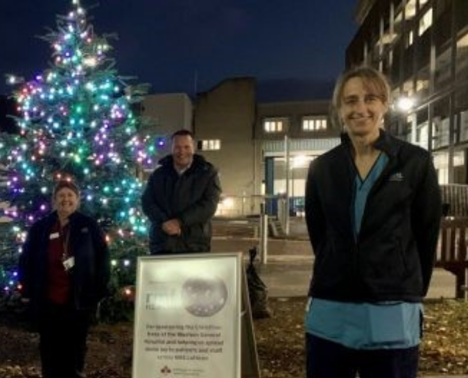 Nurses standing in front of a lit Christmas tree in the hospital grounds