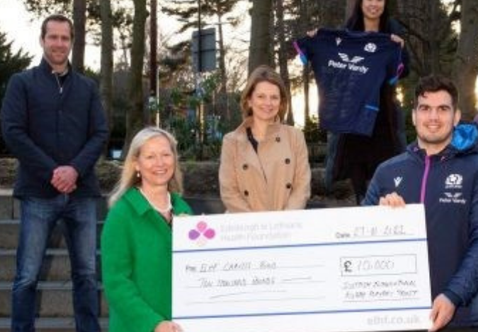 Two rugby players and hospital staff with a large cheque