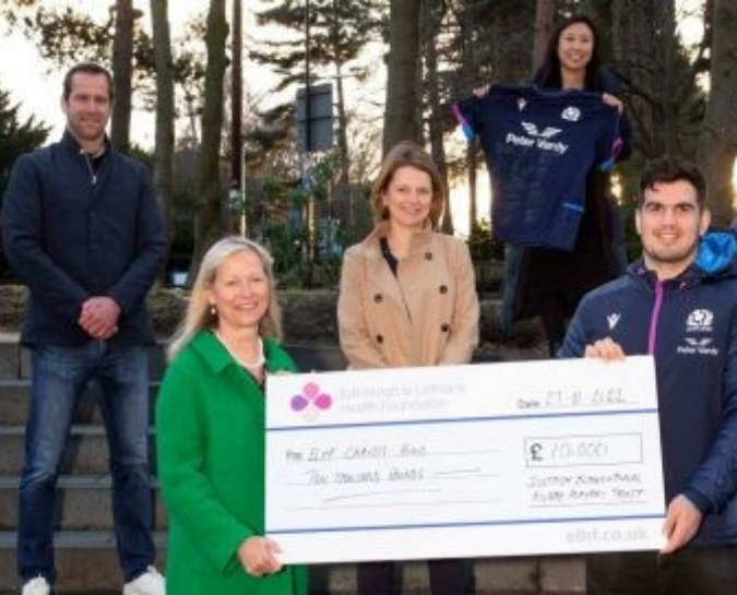 Two rugby players and hospital staff with a large cheque