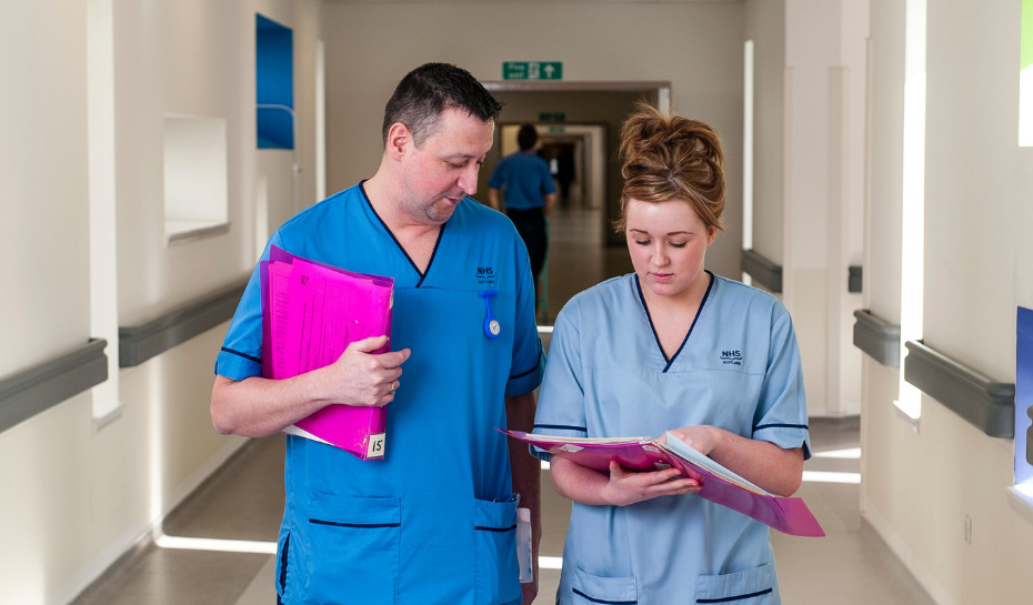 Two nurses walking down the corridor looking at a page in a folder