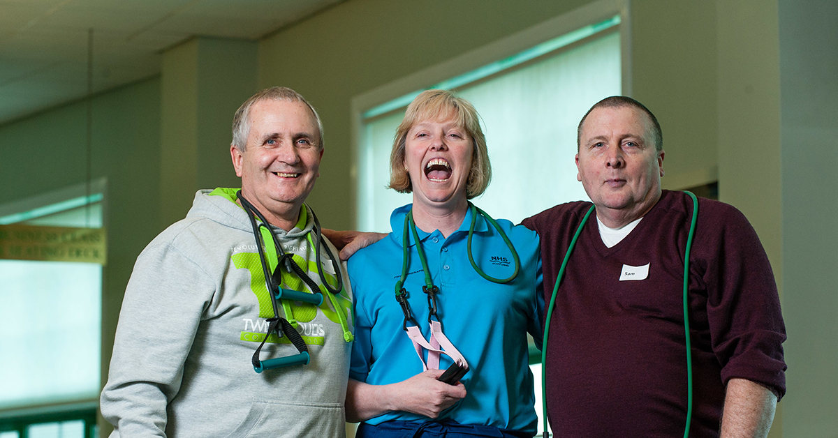 Hospital staff with fitness equipment hanging on shoulders embracing and smiling