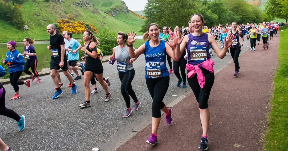 Two girls smiling and waving as they run the Edinburgh Marathon