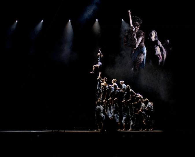 Performers on a stage standing three people high on shoulders with dark lighting