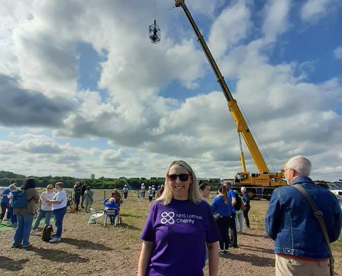 An NHS Lothian Charity Champions smiling at the camera near the beginning of the zipslide wearing a purple NHS Lothian Charity purple t-shirt.