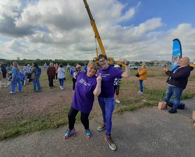 Two NHS Lothian Charity Champions stood near the beginning of the zipslide with their thumbs up smiling whilst wearing their NHS Lothian Charity purple t-shirt.