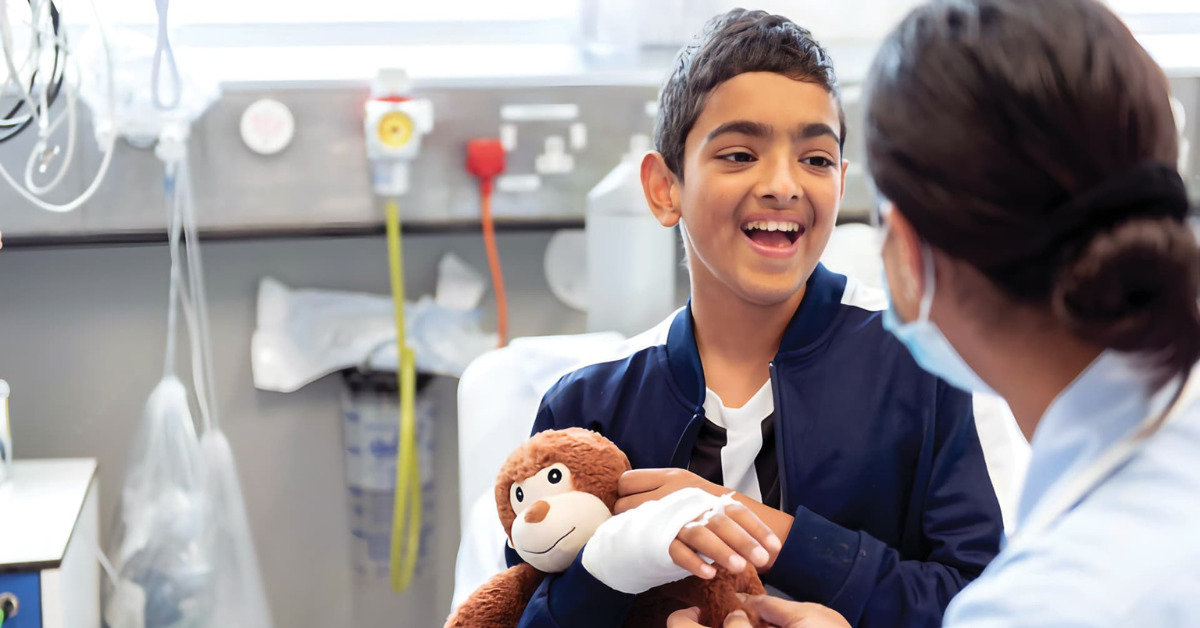 Boy smiling at the camera with a bandage on his arm cuddling a monkey