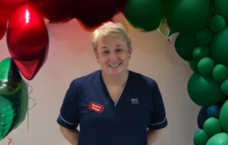 Leza, Senior Charge Nurse at the Royal Hospital for Children and Young People smiling at the camera stood in front of a balloon arch