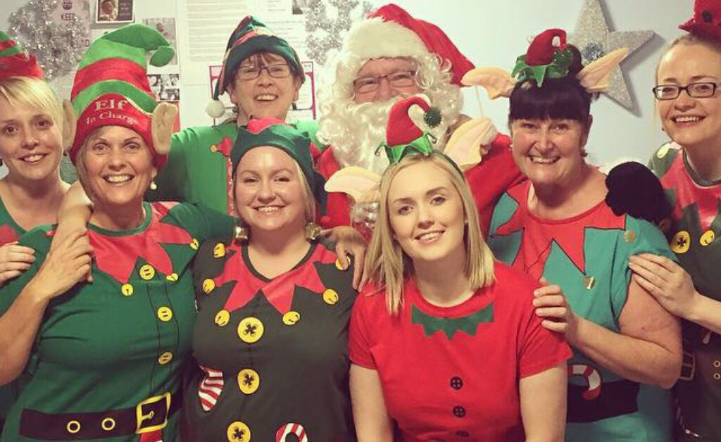 7 members of NHS Lothian staff from the Labour Ward at St Johns smiling at the camera dressed as elves with Santa