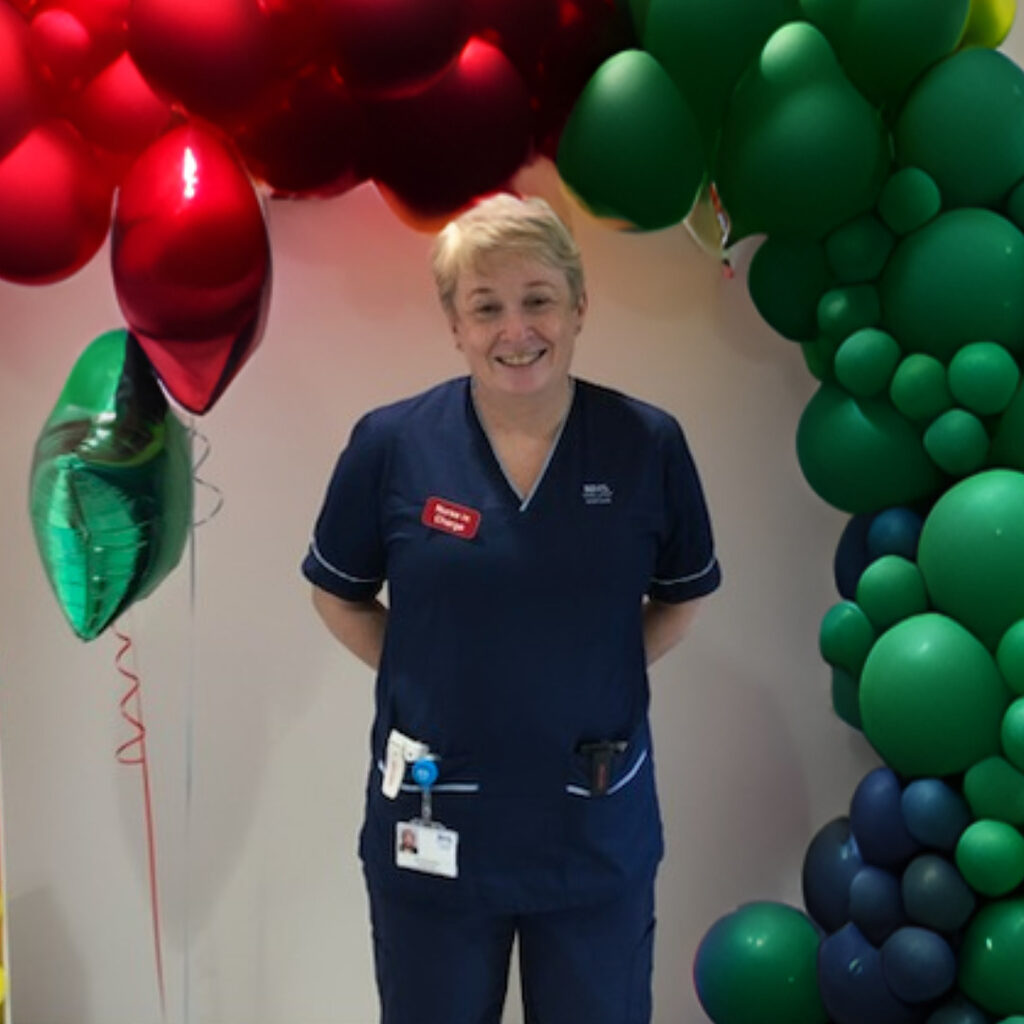 Leza, Senior Charge Nurse at the Royal Hospital for Children and Young People smiling at the camera stood in front of a balloon arch