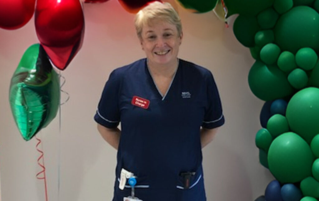 Leza, Senior Charge Nurse at the Royal Hospital for Children and Young People smiling at the camera stood in front of a balloon arch