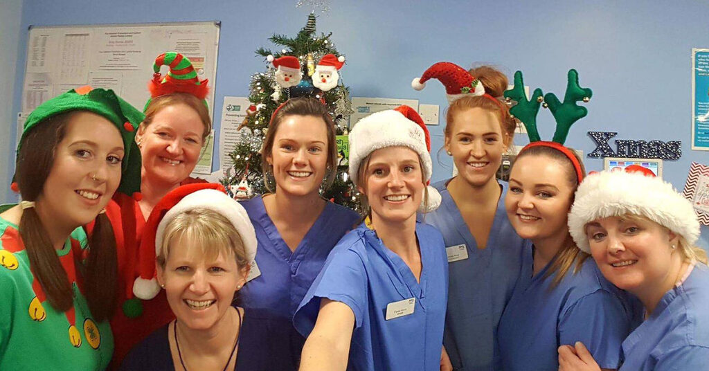 NHS Lothian staff stood together smiling at the camera wearing Santa hats, reindeer antlers and elf headbands.