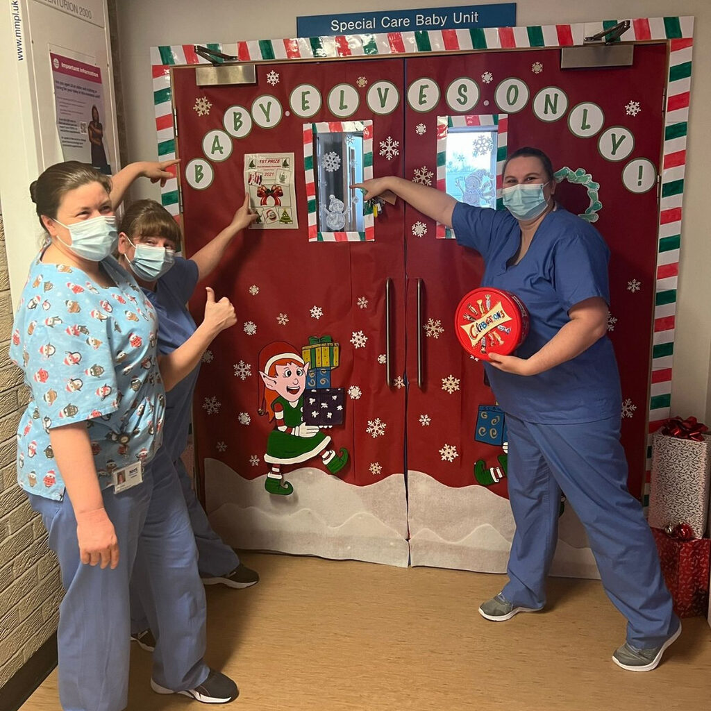 NHS Lothian staff stood by the entrance to the special care baby unit at St Johns. On the door is says "Baby Elves Only"