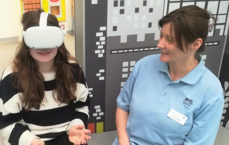 Isla watching the virtual reality film beside an NHS Lothian member of staff