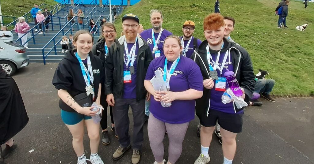 Eight Kiltwalk Charity Champions stood at the end of the Kiltwalk in their NHS Lothian t-shirts and finishers medal smiling