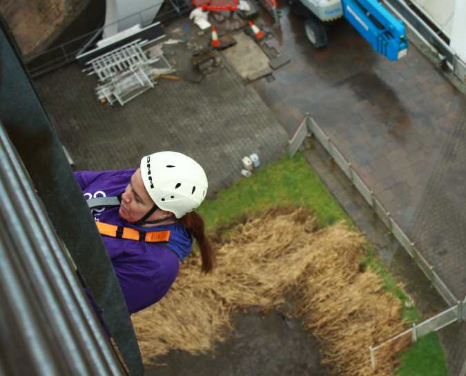 Top down view of a NHS Lothian Charity Champion starting the decent from the Falkirk Wheel Abseil. Wearing a harness, helmet and a purple NHS Lothian Charity t-shirt.