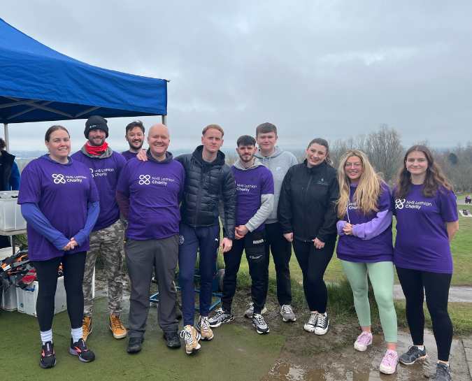10 NHS Lothian Charity Champions stood smiling at the camera after they have taken part in the abseil. Everyone is smiling and wearing their purple NHS Lothian Charity t-shirt.