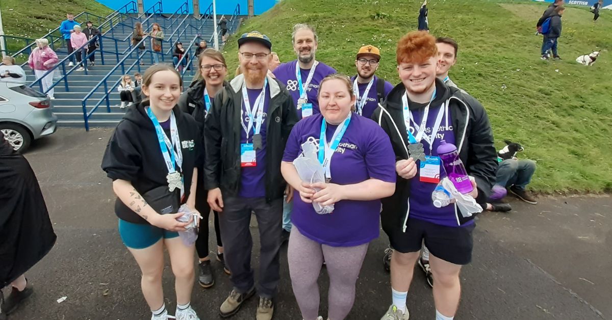Eight Kiltwalk Champions smiling at the finish wearing their medals and NHS Lothian Charity purple t-shirts