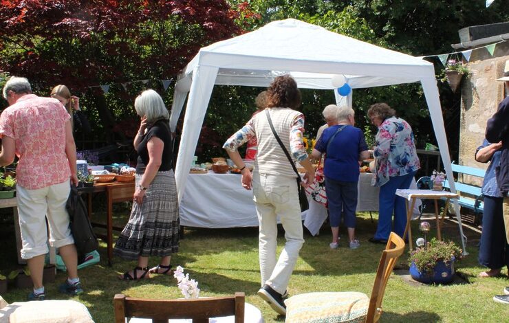 Photo of a garden with a marquees. People are walking around looking at the NHS Big Tea stalls and chatting.