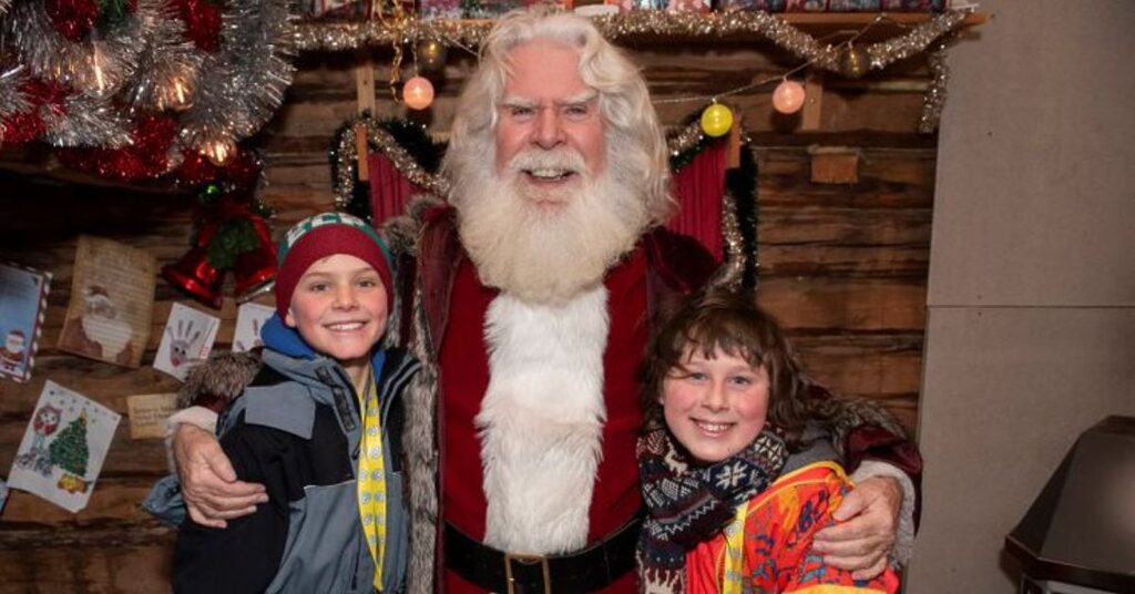 Santa smiling with two children in Lapland at Christmas during the FACE annual trip to support families impacted by cancer