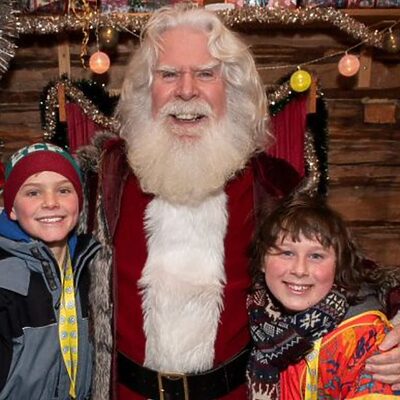 Santa smiling with two children in Lapland at Christmas during the FACE annual trip to support families impacted by cancer