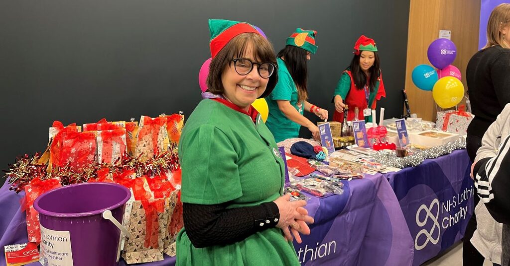 Woman smiling at the camera wearing a green elf costume and green and red hat.