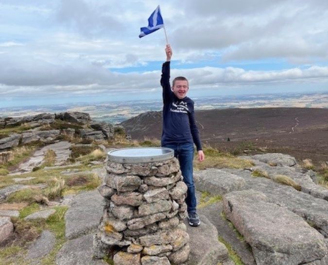 Fundraiser, Findlay Bain, at the top of Bennachie waving a flag