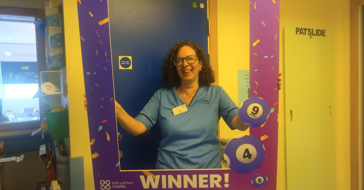 lottery winner, Sylvia, in front of a blue door in the hospital holding up the lottery winner frame