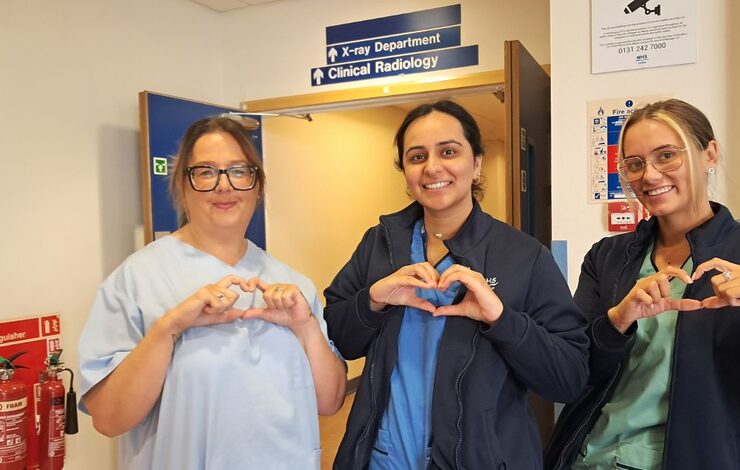 three members of staff in NHS uniforms facing the camera and making heart shapes with their hands