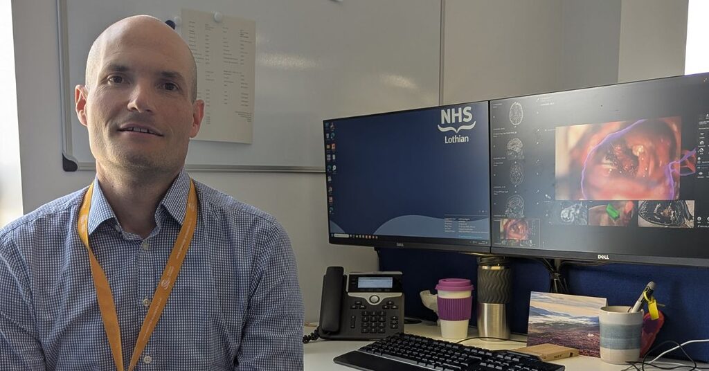Mr Anthony Wiggans beside a computer showing the brainlab software