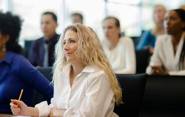 A woman listening at a conference, facing forward taking notes