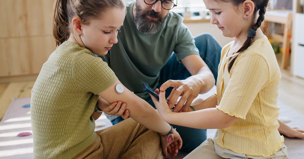 parent showing children how to use a diabetes monitor