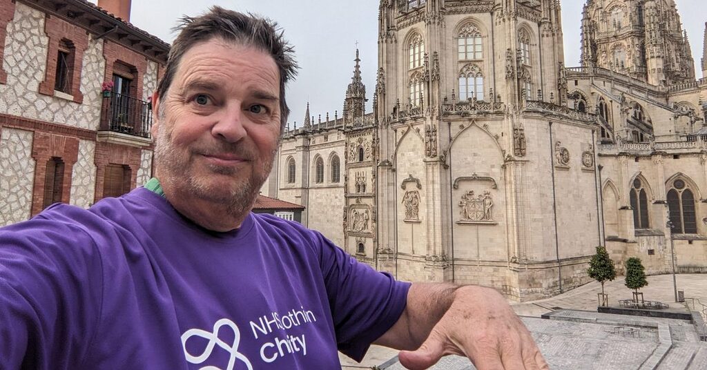 Alan McEwan walking the Camino de Santiago smiling for the camera in his NHS Lothian Charity t-shirt