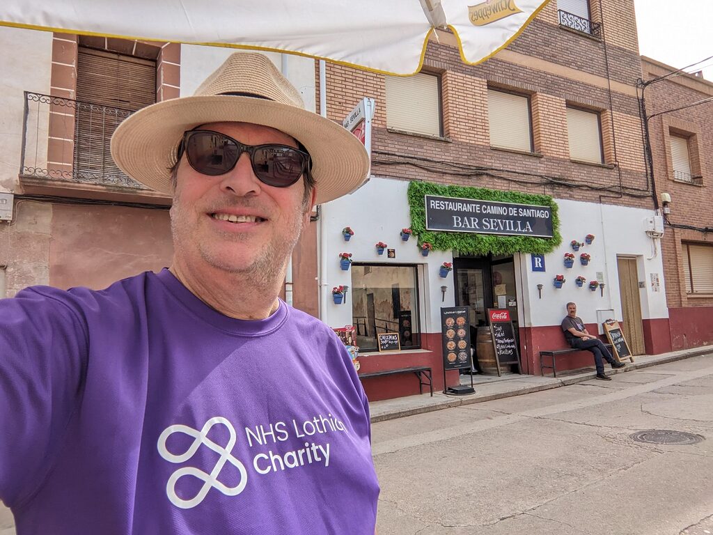 Alan McEwan walking the Camino de Santiago smiling for the camera in his NHS Lothian Charity t-shirt