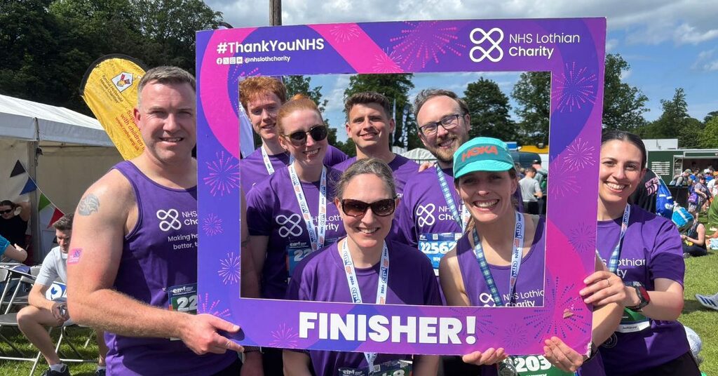 a group of NHS Lothian staff in NHS Lothian Charity t-shirts holding a sign saying 'Finisher' after completing the Hairy Haggis Relay at the Edinburgh International Festival