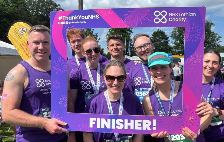 a group of NHS Lothian staff in NHS Lothian Charity t-shirts holding a sign saying 'Finisher' after completing the Hairy Haggis Relay at the Edinburgh International Festival