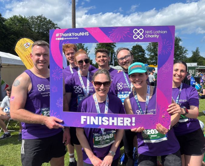 a group of people in NHS Lothian Charity t-shirts standing behind an NHS Lothian Charity finishers frame