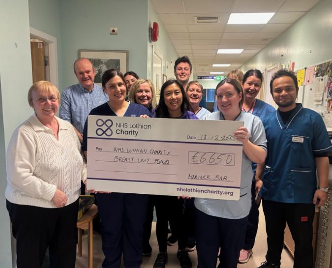 a group of people including NHS Lothian Staff in a hospital corridor holding up a big cheque