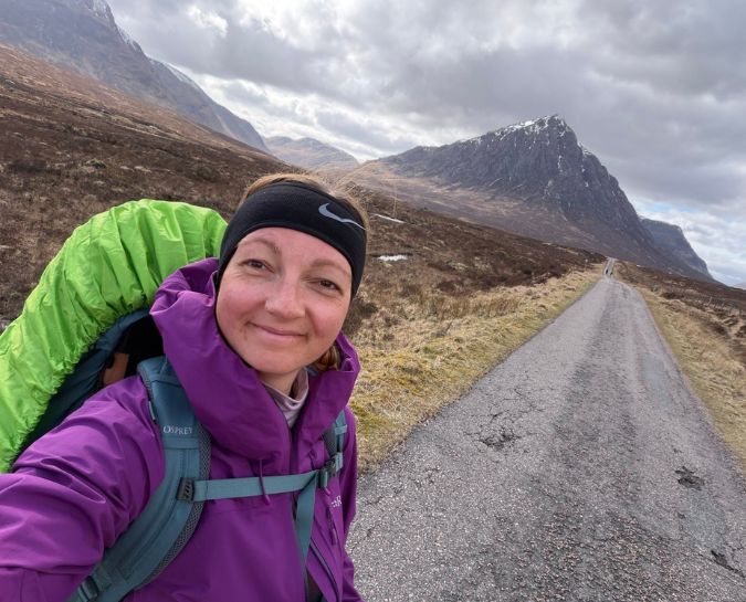 a woman with a rucksack taking a selfie with a hill behind her