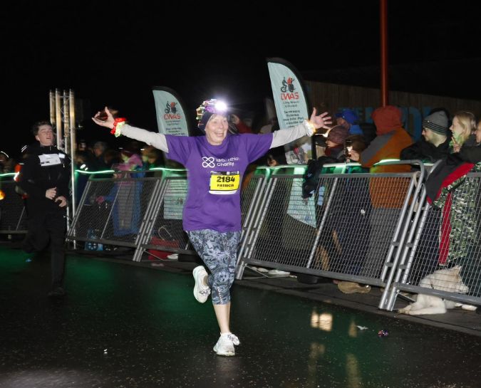 a woman in an NHS Lothian Charity t-shirt and head torch running with her arms open